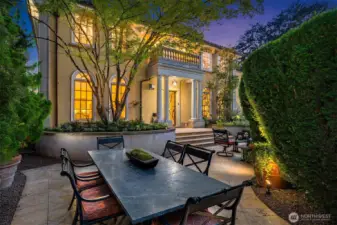 The lovely front courtyard features a large stone patio with dining and seating areas surrounded by thick privacy hedges.