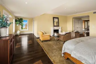 Perspective of spacious primary bedroom with seating area around the marble gas fireplace.
