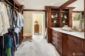 Primary walk-in closet with fine, custom built-in organizers and dresser with Carrara marble countertop and mirror.