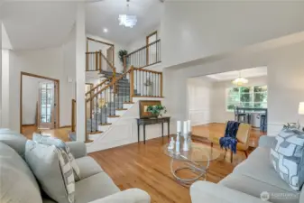 The formal living room showcases the home's elegance with a stunning view of the grand staircase and a beautiful chandelier. Natural light highlights the spacious layout and timeless design elements.