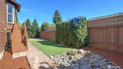 Enjoy low-maintenance living in this private, fully fenced backyard retreat. Featuring lush turf grass, a stamped concrete walkway, and mature landscaping, this space is ideal for entertaining or relaxing outdoors. A charming rock garden adds visual interest, while the tall evergreens and lattice-topped fencing provide added privacy. Whether you're hosting guests or unwinding with a book, this thoughtfully designed outdoor area offers the perfect blend of beauty and function.
