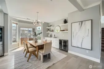 Entertain in style in this beautifully curated dining area that seamlessly blends form and function. Bathed in natural light from a charming bay window and sliding glass doors, the space features wide-plank hardwood floors and a contemporary light fixture that makes a bold statement. A custom built-in buffet with floating shelves and a dual-zone wine fridge provides both storage and flair, perfect for displaying your favorite décor or hosting with ease. The warm wood dining table and soft, neutral-toned chairs add an inviting touch, making this an ideal setting for intimate dinners or lively gatherings.