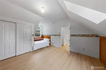 The second upper-level bedroom mirrors the thoughtful built-ins, featuring a custom storage bed with drawers, spacious layout, and a skylight that fills the room with natural light. A playful custom accent wallpaper adds personality and warmth.