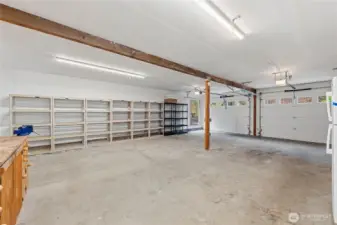 Oversized attached garage with two car doors offering ample space for vehicles, storage, or a workshop setup. The generous depth allows for flexible tandem-style parking, along with existing shelving for easy organization and storage.