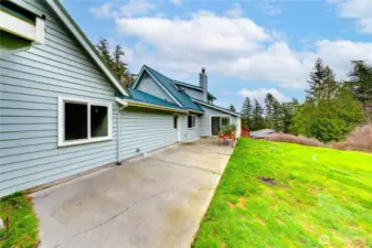 Spacious backyard showcasing the sunroom, a concrete patio area, raised garden bed for planting, and a large green lawn.
