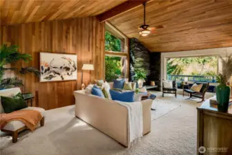The living room showcases soaring cedar ceilings, dramatic stone fireplace, and walls of windows that blur the line between indoors and nature.