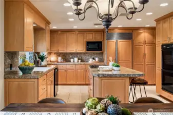 A chef’s kitchen featuring warm maple cabinetry, granite counters, a large center island with breakfast bar, and seamless flow into the dining and living areas - ideal for entertaining or casual meals.