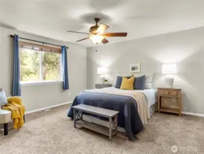 Relax in the spacious primary suite featuring soft natural light and ceiling fan comfort.