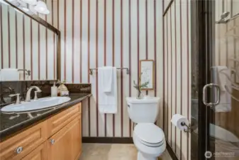 The main bathroom of the home is located in the hallway. It features stylish wallpaper, an upgraded vanity, a luxury shower with tile surround, and quality fixtures.