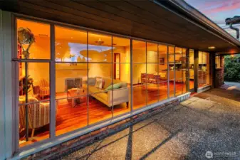 The Great Room is defined by an unusually long wall of floor-to-ceiling commercial steel windows that runs nearly the full width of the home. This dramatic span opens directly to the Lanai and East Terrace and fills the interiors with steady natural light.