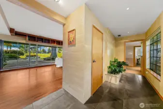 A wide hall wrapped in Venetian plaster and stone tile marks the transition from the Great Room to the bedroom wing. Floor-to-ceiling windows draw in natural light while warm wood details and clean lines underscore the home’s quiet, crafted circulation path.