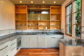 The bungalow’s full kitchen is outfitted with tailored millwork, open cedar shelving, and stainless counters that wrap the room. A two-burner Wolf cooktop, Bosch oven, and integrated refrigeration support independent living, while the large window brings in garden light that plays across the joinery. This space reflects the same level of craft found throughout the bungalow, designed for guest use, extended stays, or creative work.