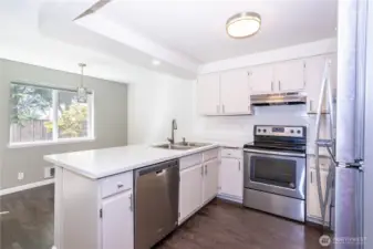 Wide kitchen view with breakfast bar, stainless appliances and wood flooring.