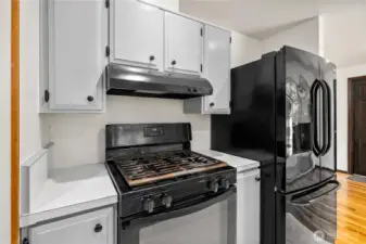 Kitchen features include a gas range with overhead vent and a sleek French-door refrigerator. Convenient layout offers efficient workspace while keeping cooking and prep zones close at hand.