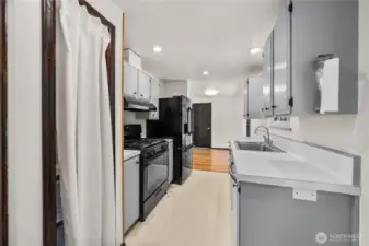 Long view of the kitchen highlighting efficient counter space, matching black appliances, and easy flow between cooking, dining, and utility areas. Functional design ideal for both everyday living and entertaining.