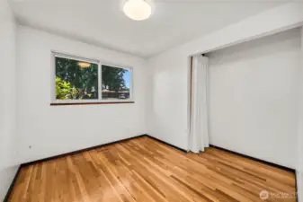 Light-filled bedroom featuring refinished hardwood floors and a wide quadruple-pane window that enhances both natural light and noise reduction. A cozy closet offers flexible storage, while neutral walls make this space easy to personalize for use as a bedroom, office, or guest room.
