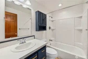 The home’s full bathroom offers a clean, functional design with a shower/tub combo featuring built-in shelving, a bright vanity with storage, and overhead lighting. Bold navy cabinetry with gold hardware provides a stylish contrast, while the neutral finishes keep the space fresh and easy to personalize.