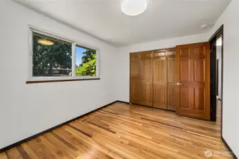 Spacious primary bedroom featuring refinished hardwood floors, a large window for natural light, and an expansive wall-to-wall closet with paneled doors for excellent storage. Neutral finishes and simple lines make this room move-in ready and easy to style as your personal retreat.