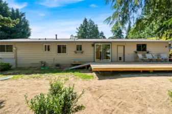 Wide view of the backyard showcasing the home’s exterior and spacious wood deck, perfect for entertaining or relaxing outdoors. Access the dining room through the sliding glass door and the garage through the single door.
