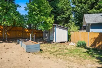 Backyard shed offers convenient storage for tools and lawn equipment, with raised garden beds ready for planting.