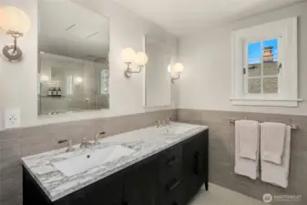 A marble-topped double vanity is paired with Waterworks fixtures and globe sconces. Penny-tile (heated) flooring,  and a glass-enclosed walk-in shower (with digital thermometer) complete this spa-like primary bathroom.