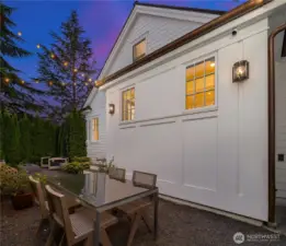 An elegant garden dining area, framed by lush evergreens and glowing café lights, offers the perfect setting for al fresco meals long into the evening.