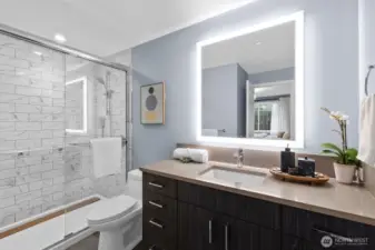 Spacious tiled shower with LED mirror.