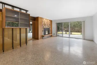 The family room boasts large windows, terrazzo floors, the other side of the dual fireplace, and oversized sliding doors leading to the spacious backyard.