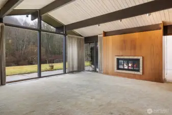 The entryway seamlessly flows into the living room, boasting vaulted ceilings, exposed beams, and a striking dual-sided wood-burning fireplace.