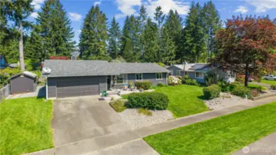 Striking front view highlights a double-car garage, wide driveway, and freshly painted exterior complemented by manicured hedges and a garden shed.
