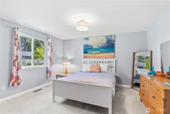 Expansive primary bedroom with soft natural light, calming gray walls, and plush carpeting. Features a spacious layout, large window with private backyard views, and stylish touches including bold drapery and coastal-themed décor. A perfect retreat to unwind in comfort.