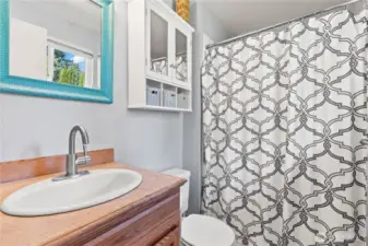 Fresh and functional full bathroom featuring a stylish vanity with updated faucet, built-in wall cabinet for added storage, and a tub/shower combo with modern patterned curtain. Natural light and thoughtful accents add charm to this everyday essential space.