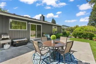 Step into serenity—this photo showcases the patio's functionality, from grilling to lounging, with beautifully maintained landscaping and plenty of room to entertain. The backdrop of evergreens adds to the Northwest charm and sense of peace.