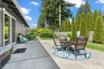 A closer look at the charming patio setup, complete with a shaded dining area and cozy seating space. This outdoor retreat is perfect for al fresco meals or winding down in the tranquility of your private backyard oasis.