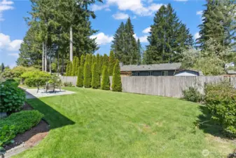 This expansive backyard offers a lush, green lawn bordered by mature trees and a privacy fence—ideal for pets, playtime, or even a garden expansion. The tall arborvitae provides a beautiful natural screen, enhancing both beauty and seclusion.