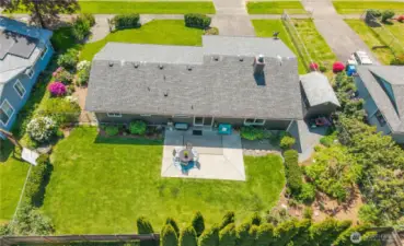 Stunning drone capture of the backyard oasis featuring a spacious concrete patio for outdoor dining, lush green lawn, and mature privacy landscaping. Thoughtfully designed with garden beds, flowering shrubs, and peaceful seating areas—perfect for entertaining or relaxing under the sun.