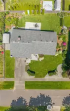 Bird’s-eye view showcasing the expansive, fully landscaped lot with lush green lawn, dual patios (front paver and rear concrete), mature trees, and privacy hedging. This overhead drone shot highlights the layout of the home, backyard entertaining space, garden beds, and overall curb appeal.