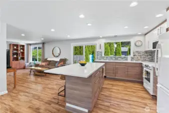 Step into a chef-inspired kitchen featuring a stunning quartz waterfall island, custom soft-close cabinetry, and full tile backsplash. Enjoy open sight lines to the cozy living area and views of the landscaped backyard through oversized windows and a sliding glass door—perfect for entertaining or relaxing in style.