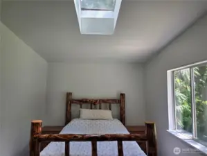 Primary bedroom has skylight for additional lighting. The room is large enough to easily accommodate this queen size bed with end tables.