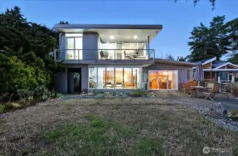 Exterior back view of this Mid-Century Modern-inspired, 2-story beachfront residence at dusk.