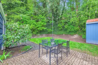 Patio beyond the covered deck with outdoor deck lights. Storage shed and lawn in the background.