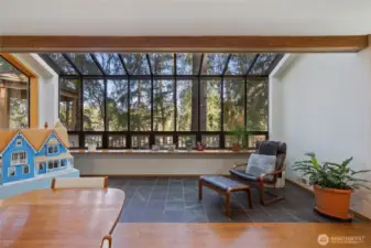 Sun-filled solarium-style seating area with floor-to-ceiling windows, offering peaceful forest views and a perfect space for relaxation or reading.